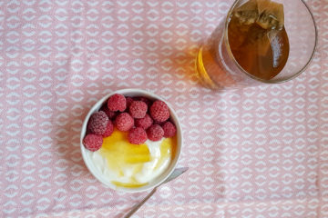 petit bol de fromage blanc recouvert de framboises et miel avec un verre de thé