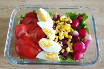 Lunchbox avec des oeufs durs, de la salade, des haricots rouges, du maïs, de la tomate et des radis